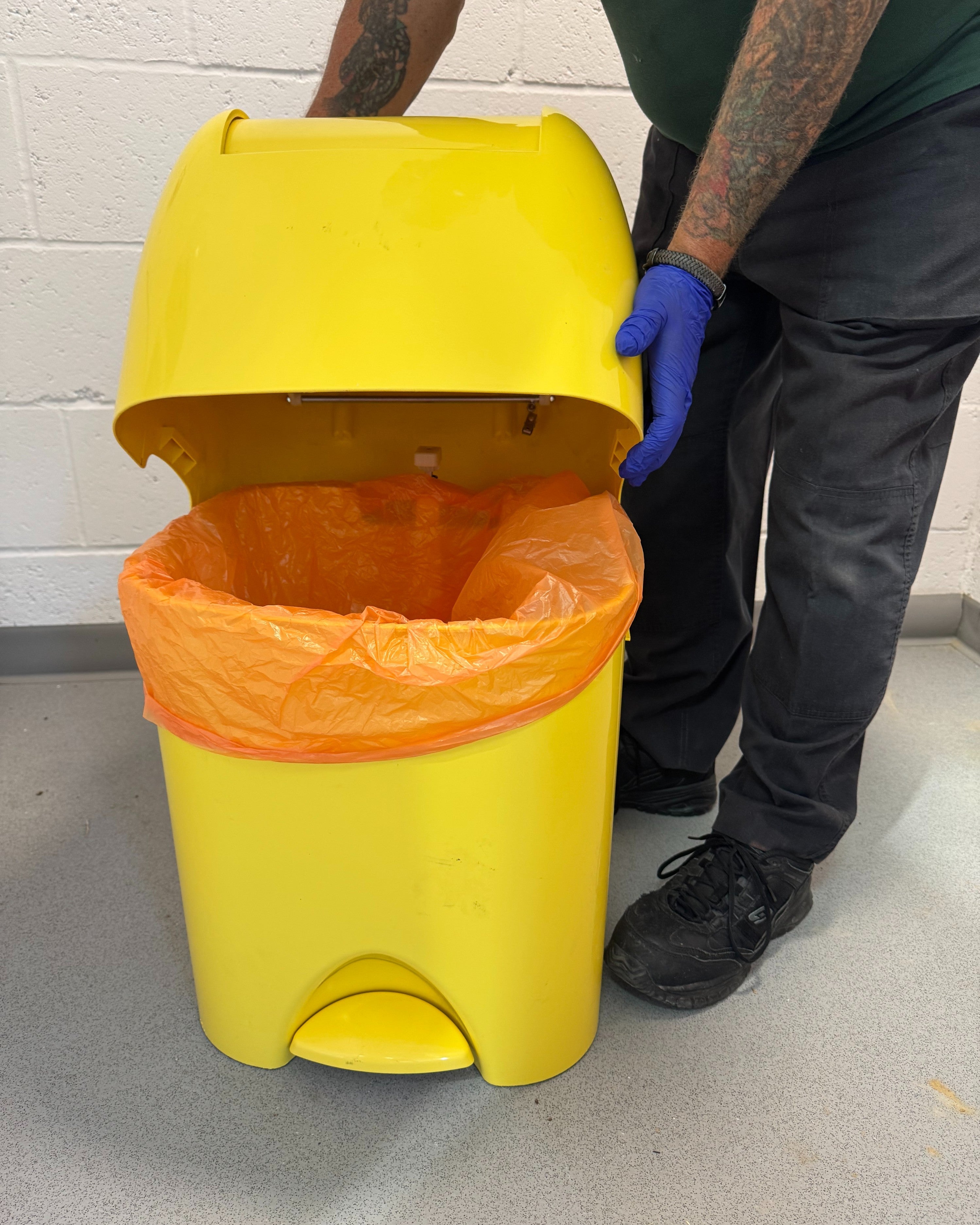 Hazardous waste disposal: engineer holding a yellow medical disposal unit with an orange hazardous waste bag