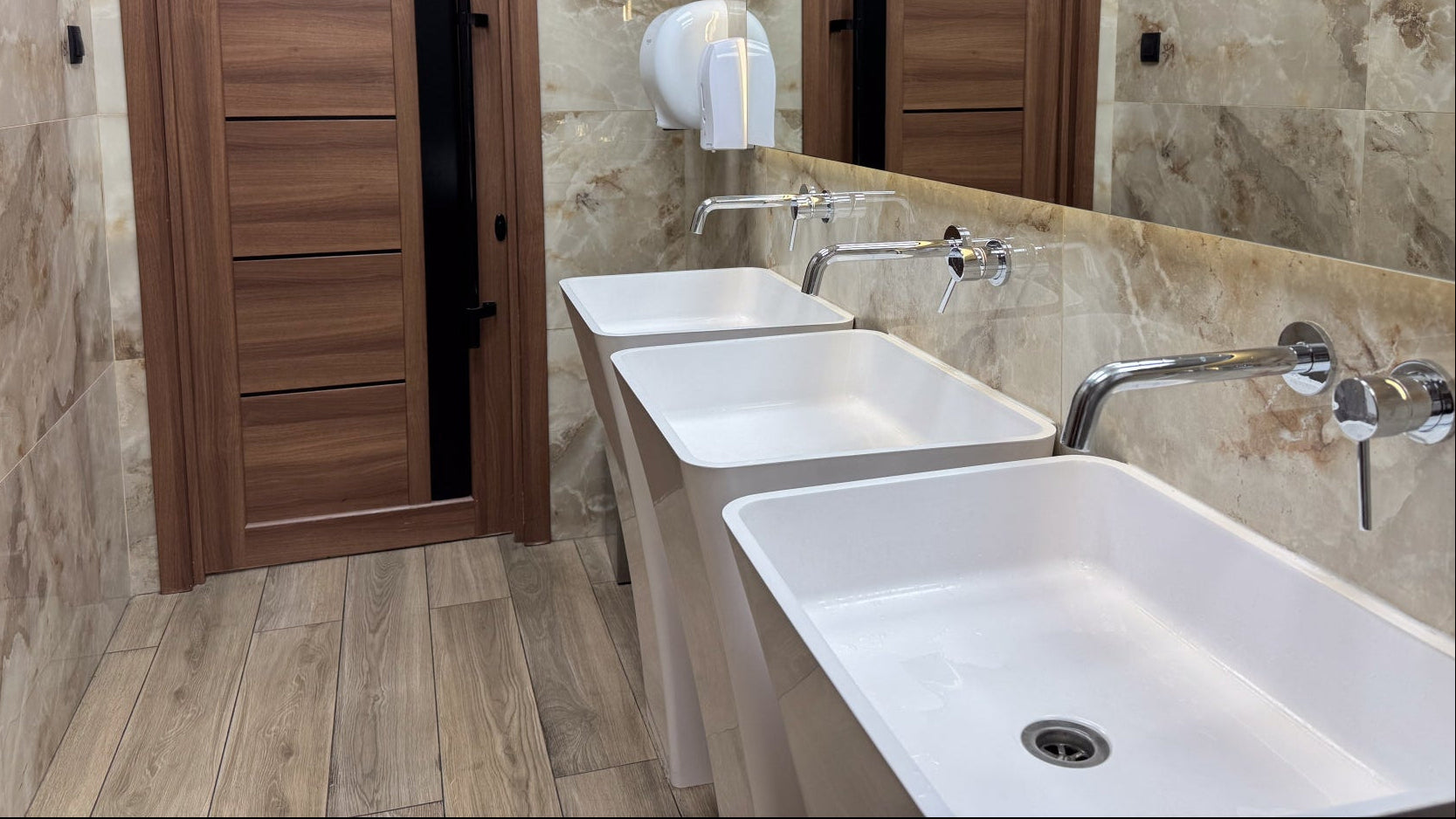 Hand towel dispensers in a washroom with a row of sinks and a mirror