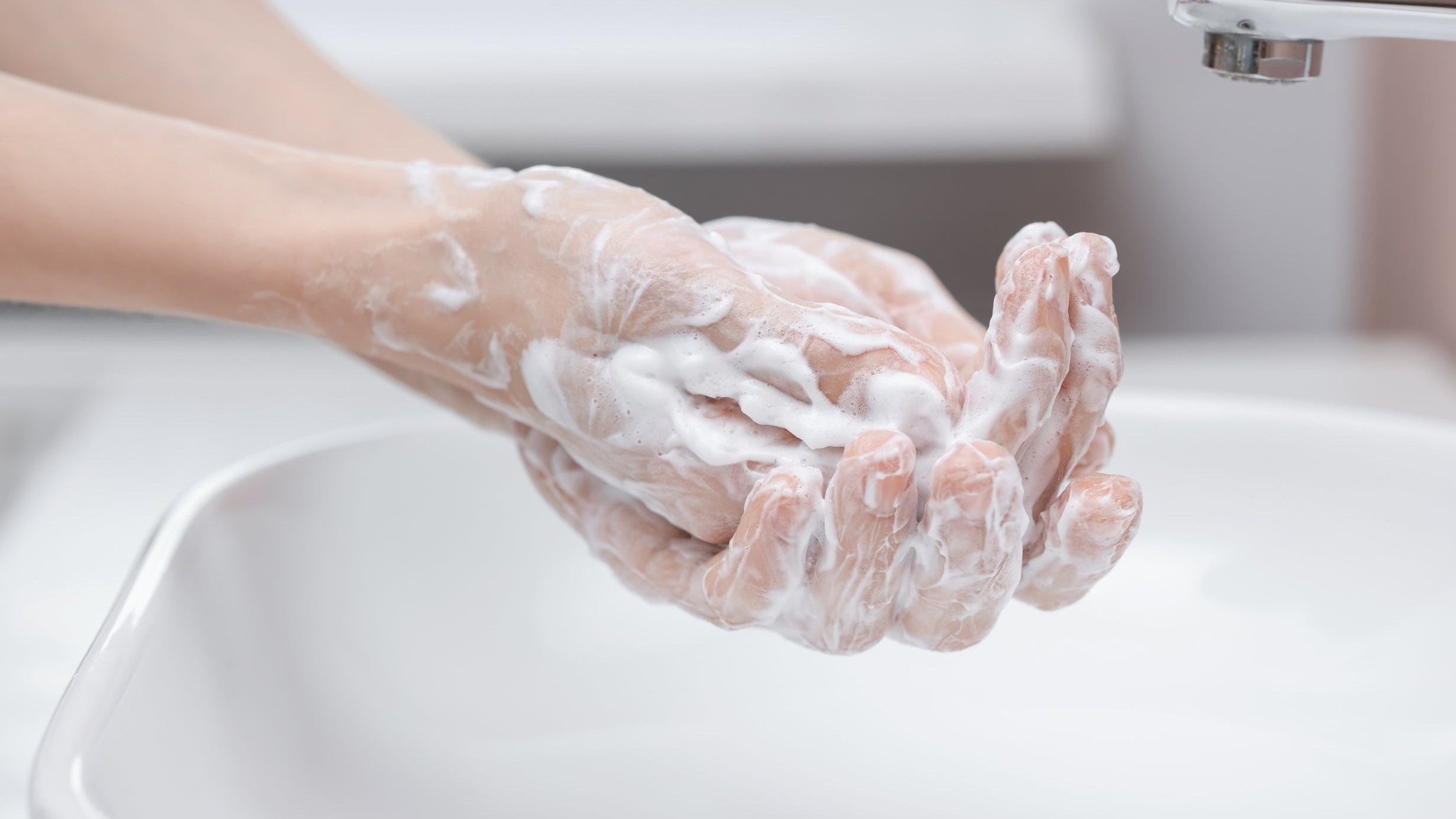 Soap dispensers: hands being washed with soap at a washroom sink